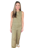 A woman modeling a sleeveless olive green jumpsuit with front flap pockets, shown against a plain white background.