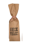 A brown kraft paper gift bag tied with red-and-white string, printed with the words 'HECK YEAH!' in black stencil-style lettering, shown on a plain white background.