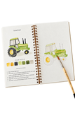 An open spiral-bound art journal or sketchbook showing a watercolor tractor illustration, a color palette strip, and printed instructions, with a paintbrush resting on the page against a white background.