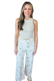 A woman modeling a sleeveless light beige crop top and white wide-leg pants with a small multicolor bird print, set against a plain white background.