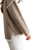 A close-up side view of a person wearing a taupe knit sweater with white contrast trim and white pants against a plain white background.