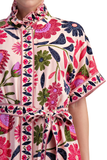 A close-up of a short-sleeve collared dress with a colorful floral and paisley print on a light pink base, featuring a matching tie belt at the waist.