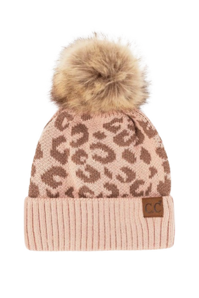 light pink beanie, with tan leopard spots. Beanie hat has brown and tan faux fur pom pom on the top. Beanie has a solid light pink ribbed fold over with a tan leather patch that reads CC on it.