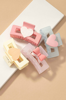 Assorted rectangle shaped frosted acrylic hair claw clips on a tan and white background. Color of hair claws include: Pink with a white heart, Blue with a pink heart, purple with a pink bow, and cream with a tan heart. 