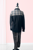 Mannequin showing the back of a black denim and plaid shacket. Shacket is black denim, with a black collar and gray. black, tan and white plaid detailing across the back of the shacket. Mannequin is also wearing gray suede leggings