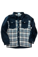Black denim button up shacket with 2 front button closure breast pockets, and a brown, gray, and white plaid material on the front panel starting at the breast pocket down and along the top shoulder of the shacket. Shacket has silver buttons on the breast pockets, wrist and along the front center of the shacket. 