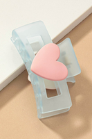 Blue frosted acrylic hair claw clip with a light pink matte heart in the middle. Hair claw is pictured on its side on a pink and tan background.