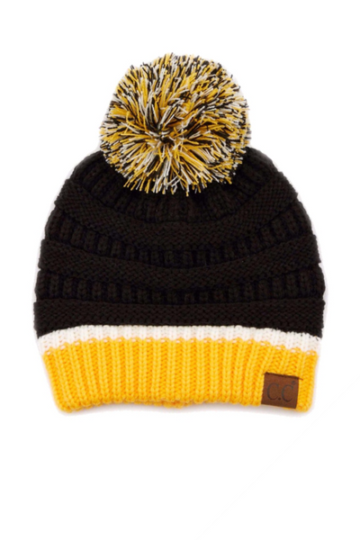 Knited C.C. beanie on a white background. Beanie as has a string pompom with white, yellow and black thread. Beanie has a yellow band at the bottom, then a white stripe and the remainder of the cap is black
