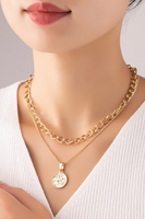Two piece necklace set on a woman’s neck. First gold necklace has a simple chain with a circular coin like pendant. The other chain is a shorter link chain.