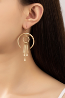 Gold crescent shaped dangling earrings with a circular charm hanging from the crescent, 4 gold stick shaped tassels and hanging from the hollow circle. Earring is shown worn on a women's ear.