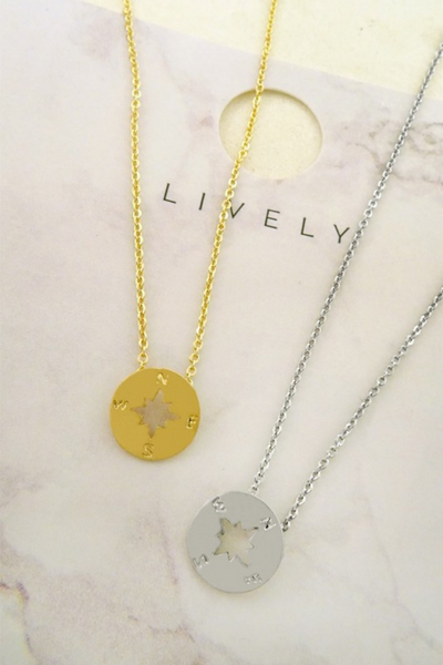 Gold and silver necklaces pictured on a jewelry card. Both necklaces have a dainty compass charm. Compass is a nautical medallion disk type of compass  