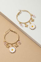Gold hoop earrings on a white tile laying on a tan background. Gold hoop earrings have 5 dangling charms. Charms include: an enamel daisy, 2 gold bees, and 2 picks beads.