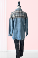 Back side of a blue denim & plaid shacket on a mannequin. Shacket has a denim blue collar, plaid detailing along the back and onto the shoulders. Plaid detailing is gray, white and brown. Frayed detailing not he bottom of the shacket and along the plaid back detailing