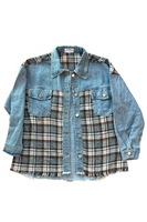 Blue denim button up shacket with 2 front button closure breast pockets, and a brown, gray, and white plaid material on the front panel starting at the breast pocket down and along the top shoulder of the shacket. Shacket has silver buttons on the breast pockets, wrist and along the front center of the shacket. Shacket has a frayed hem bottom.