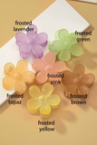 Frosted colored daisy hair claw clips on a white and tan background. Colors include: lavender, green,  orange, brown, pink and yellow 