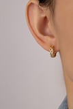 gold braided huggie style earring shown on an earlobe