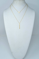 Gold layered necklace on a white mannequin neck/chest stand. Gold necklace is one necklace but has  two layered chains. First chain has a gold circle, second chain has a gold bar. 
