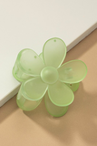 Up close photo of a frosted lime green daisy hair claw clip on a white and tan background