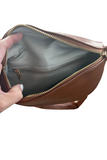 Inside of a camel faux leather bum bag. Inside of the bag is lined with a pattern material. Interior zipper closure is shown.