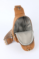 Inside of the camel faux leather crossbody sling bag, part of the white and tan patterned guitar strap is shown. 