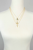 Three row gold chain necklace that is one necklace. Each layered chain has a different charms. Charms include a gold locket with a blue bead, a sun with a white stone center, and a white bullhorn with gold and gemstone detailing on a white mannequin 