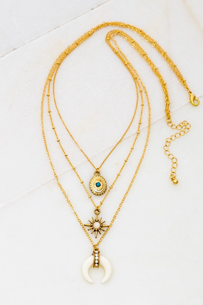 Three row gold chain necklace that is one necklace. Each layered chain has a different charms. Charms include a gold locket with a blue bead, a sun with a white stone center, and a white bullhorn with gold and gemstone detailing.