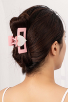 Pink rectangular acrylic hair claw clip with a white heart in the middle. Hair claw is pictured being worn on a woman with brown hair 