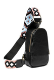 Side view of Black faux leather crossbody sling bag, part of the white, black, pink and turquoise aztec patterned guitar strap shown.