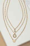 Three piece gold necklace set featuring smile face charms.  Necklaces are all individual necklaces. First necklace has an oval clear rhinestone charm, the second necklace has a rhinestone smile face charm, the third necklace has a gold smile face charm.