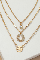 Up close photo of three gold necklaces. The shortest necklace has a oval rhinestone charm, the second necklace has a rhinestone smile face charm, the third necklace has a gold smile face charm.